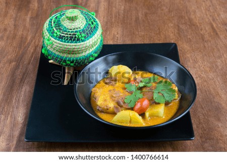 Thaï Food: Massaman Gai, curry massaman chicken with rice, served with a small traditional basket for rice - on a wooden table.