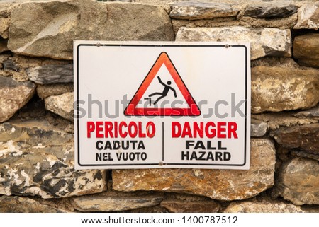 Close-up of a danger sign hung on an old stone wall warning of the risk of fall, Vernazza, Liguria, Italy