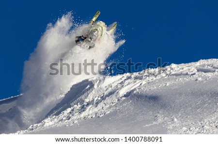 snowmobile jump straight up. the guy is flying and jumping on a snowmobile on a background of blue sky leaving a trail of splashes of white snow. bright snowmobile and suit. No brands. extra quality Royalty-Free Stock Photo #1400788091