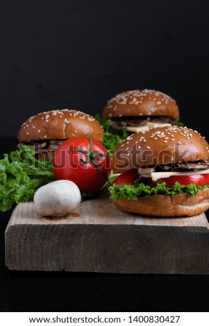 cheeseburgers with fried mushrooms, tomato and salad leaves on wooden board, vertical photo