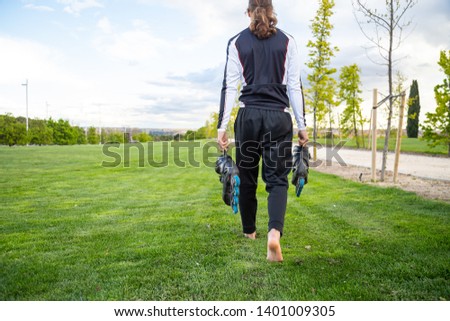 Back view of young barefoot male in sportswear with roller skates in hand walking in park