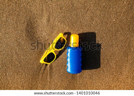 Sunscreens with sunglasses on clear sea sand on sea background. Summer vacation