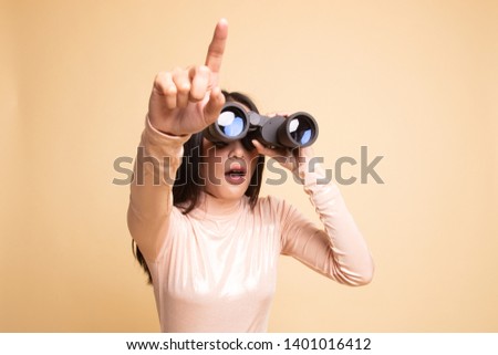 Young Asian woman  point and look with binoculars on  beige background