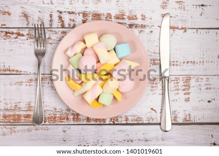 Pink plate with marshmallow on white wooden background. Fork, knife and plate on white wooden background. Top view.