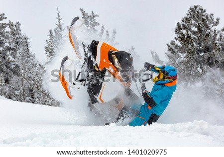 snowmobile breaks out of the snow. close-up of a sports snowmobile with a pilot on a background of gray snow-covered forest. bright snowmobile and suit without brands. extra high quality Royalty-Free Stock Photo #1401020975