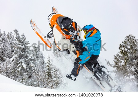 snowmobile breaks out of the snow. close-up of a sports snowmobile with a pilot on a background of gray snow-covered forest. bright snowmobile and suit without brands. extra high quality Royalty-Free Stock Photo #1401020978