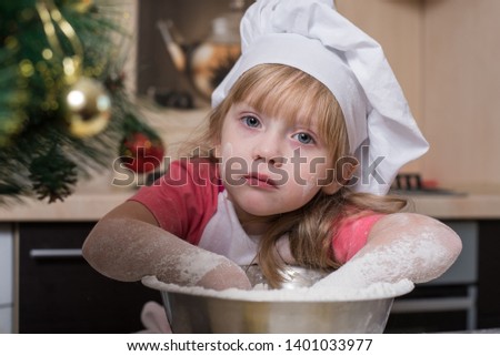Happy child in chef's hat kneading dough for Christmas cake. Portrait of a little girl cook.