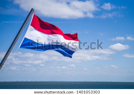 Waving flag of the Netherlands fixed to yacht mast with blue sky with white clouds and sea on background 