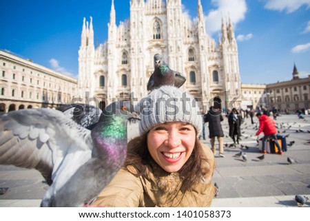 Travel, holidays and winter vacations concept - Happy young woman take selfie photo with funny pigeons in front of Duomo Milan Cathedral