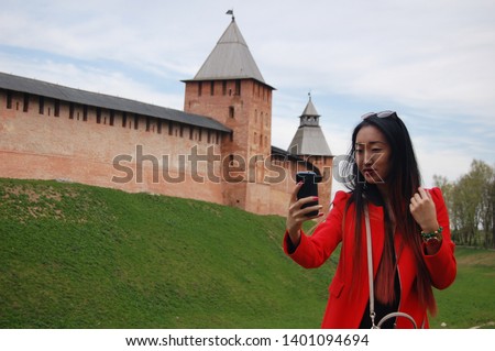 Young asian woman in red coat taking selfie by phone in front of old castle wall