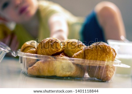 Happy child having breakfast at home. Cute healthy kid boy eating croissant and drinking yogurt. Freshly baked. Breakfast table fruit and bread croisant.