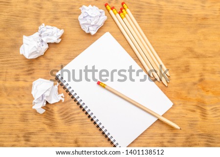 White note pad on a wooden table. Around the notepads lies lot crumpled paper