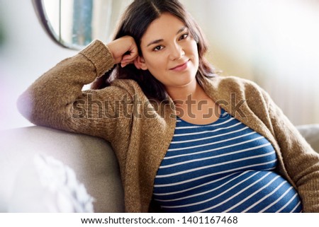 Portrait of a smiling young pregnant woman relaxing on her living room sofa at home