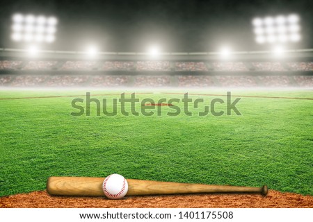Baseball bat and ball on field at brightly lit outdoor stadium. Focus on foreground and shallow depth of field on background and copy space.