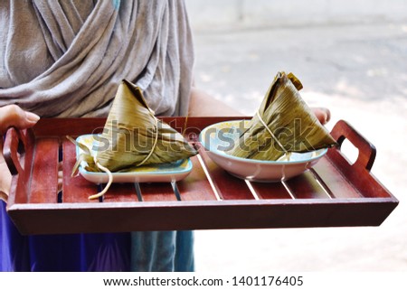 Hand holding wooden tray of zongzi, traditional homemade Chinese food for Dragon Boat festival in fifth month of every year, sticky rice dumpling with ingredients wrapped in bamboo leaf  