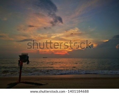 Silhouette of camera and tripod facing sunrise at sandy beach