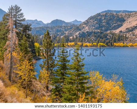 Colorful autumn landscape of June Lake, California. Blue waters surrounded by mountains, pine trees and yellow aspens. Small houses and fishing boat in the distance. Shot on a sunny day in October.
