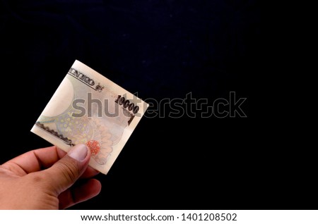 Hold a Japanese yen currency by hand on black background. Selective focus.