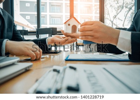 Real estate agents holding model house and automatic stamp for submit documents for customers to sign for a sale contract,real estate concept.