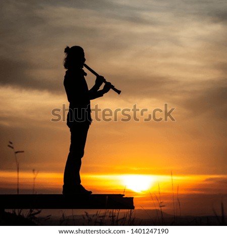 the silhouette of a male piper playing a flute against a setting sun on an urban setting