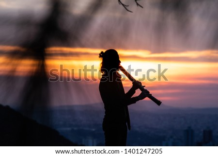 the silhouette of a male piper playing a flute against a setting sun on an urban setting