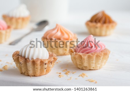 Small cakes with cream on a white table with a spoon and a mug. Selective focus. Front view.