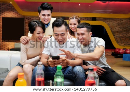 Group of friends gathered together to choose photo for uploading to social media after game of bowling