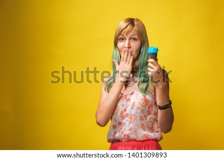Girl with light blue ice cream on a yellow background. Blonde with a cold dessert. A girl with colored hair with blue ice cream in a waffle cone.