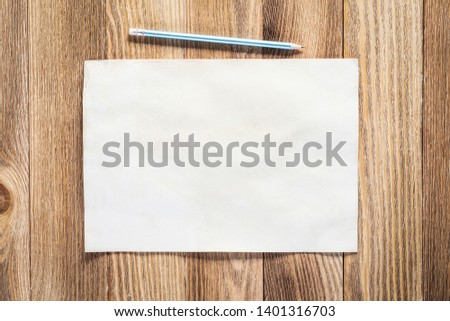 Business workspace with sheet of paper and pencil lying on wood table. View from above with copy space. Rectangular blank white paper on textured natural wooden background. Business presentation