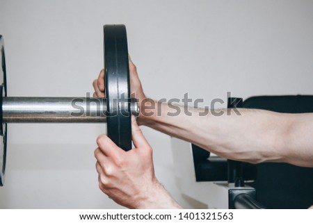 an athlete with big hands adds weight by the metal disks to the training apparatus in the training center. training equipment in the gym close-up.