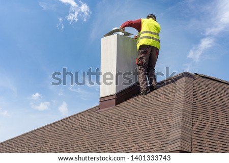 Skilled workman in protective work wear and special uniform install chimney on roof top of new house under construction Royalty-Free Stock Photo #1401333743