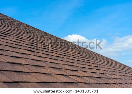 Close up photo of roof shingles installed on top of the new modern house under construction against beautiful blue sky