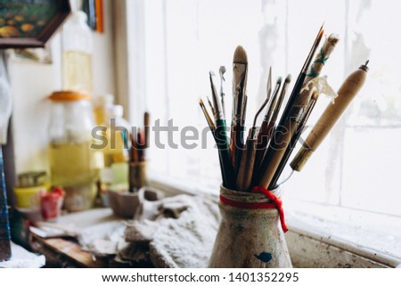 Artist's tools, brushes, paints and a palette lie on a old white wooden sills near light window background. Copy space for text