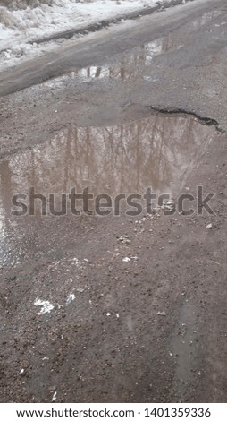 Dirt Covered Snow Melting on Side of Road Creating Puddles in Late Winter
