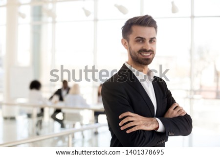 Portrait smiling employee standing with arms crossed look at camera in company office hallway, confident businessman posing for photo in modern workspace, worker in suit making picture