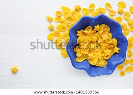 Cornflakes of different shapes in a blue cup in the shape of a flower. Close up. White wooden background. Free place. The view from the top.

