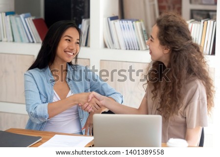 Happy multiracial girls student sit at table handshake greeting at first meeting, millennial smiling female workers shake hands get acquainted working together in office, young women reach agreement