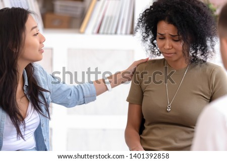 Understanding Asian girl hug show support to depressed crying african American woman at group psychological treatment, diverse stressed people undergo psychotherapy counselling or training together Royalty-Free Stock Photo #1401392858