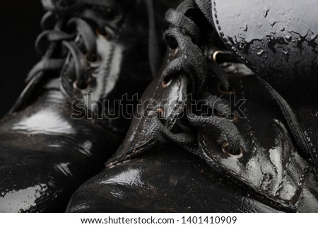 Old black army boots wet from the rain. Footwear resistant to difficult terrain conditions. Dark background.