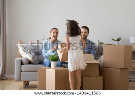Excited mother and father have fun with little daughter unpacking boxes on moving day, happy young parents laugh joke entertain with preschooler girl kid relocating to new home, playing together Royalty-Free Stock Photo #1401411566