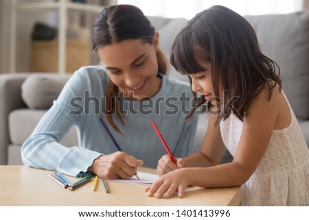 Happy young mom have fun drawing using colorful pencils with cute little daughter, smiling preschooler girl enjoy spend time painting picture with nanny, parent and kid entertain engaged in activity