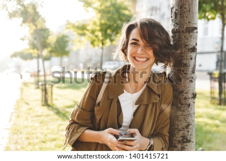 Picture of a cute young pretty woman walking outdoors in park in beautiful spring day using mobile phone.