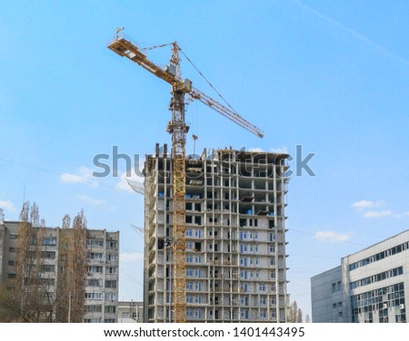 Crane builds a tall house against the blue sky .