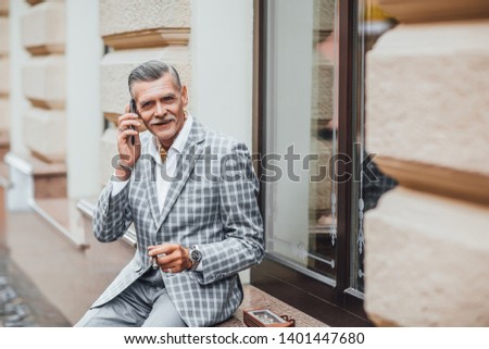What a beautiful day, stylish senior talking with his wife by phone and smoking his favourite cigarette