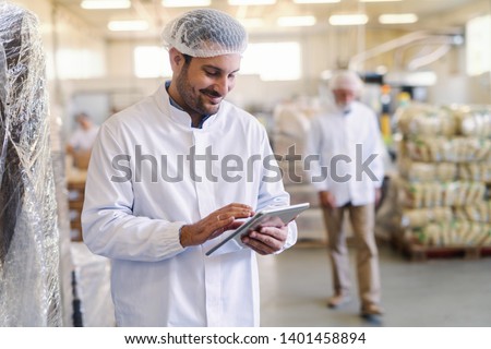 Close up of supervisor in uniform using tablet for checking data while standing in food factory.