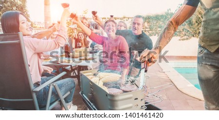 Family and friends cheering with wine, grilling meat for at bbq meal outdoor - Different age of people having fun at barbecue dinner - Summer lifestyle and fun concept - Focus on hand cooking at grill