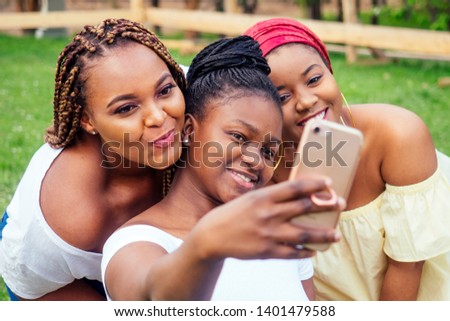 portrait of three beautiful african-american women afro braids dreadlocks and turban taking pictures of yourself on the phone in the park at a picnic,sisters on vacation