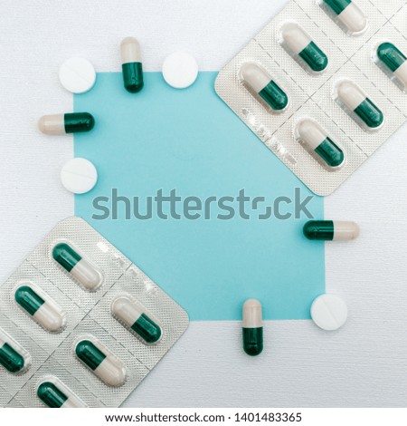 Creative layout made of variety of tablets and capsules. Flat lay. Pharmaceutical advertising background - blue square on white pearl texture background