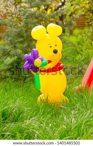 Yellow bear with flowers from balloons congratulates with a holiday in the garden on a background children's playground