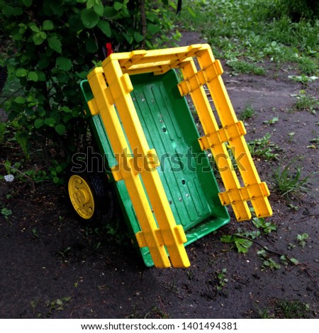 Macro photo garden kids cart. Cart trailer yellow and green. Cart on wheels. The outdoor wagon trolley cart is in the yard.